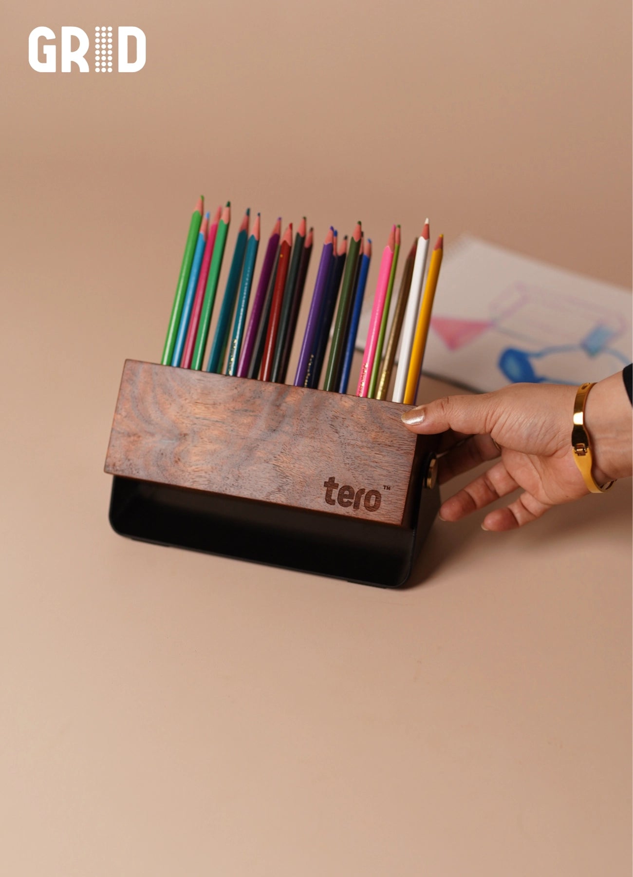 GRID solid wood pen holder with 24 slots holding pens and pencils on a desk, matte black base