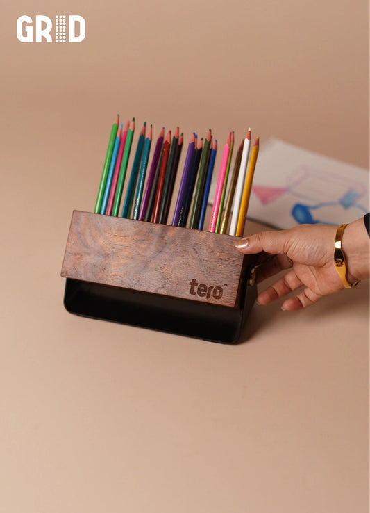 GRID solid wood pen holder with 24 slots holding pens and pencils on a desk, matte black base